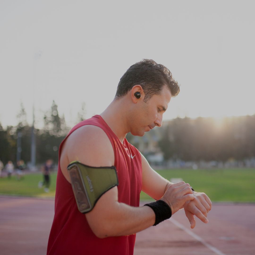 athletic man checking smartwatch during outdoor running workout at sunset